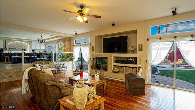 living room with hardwood / wood-style floors, ceiling fan with notable chandelier, a wealth of natural light, and a tiled fireplace