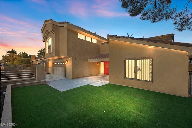 back house at dusk featuring a yard and a patio