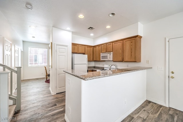 kitchen featuring light stone countertops, kitchen peninsula, a textured ceiling, white appliances, and hardwood / wood-style flooring