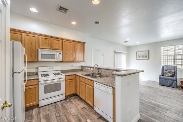 kitchen featuring kitchen peninsula, light wood-type flooring, white appliances, and sink