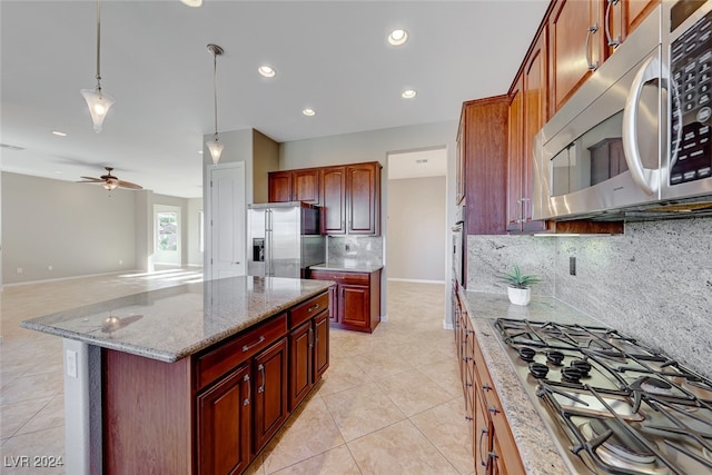 kitchen featuring light stone countertops, ceiling fan, decorative backsplash, a kitchen island, and appliances with stainless steel finishes