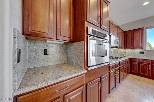 kitchen with light tile patterned flooring, light stone counters, stainless steel appliances, and tasteful backsplash