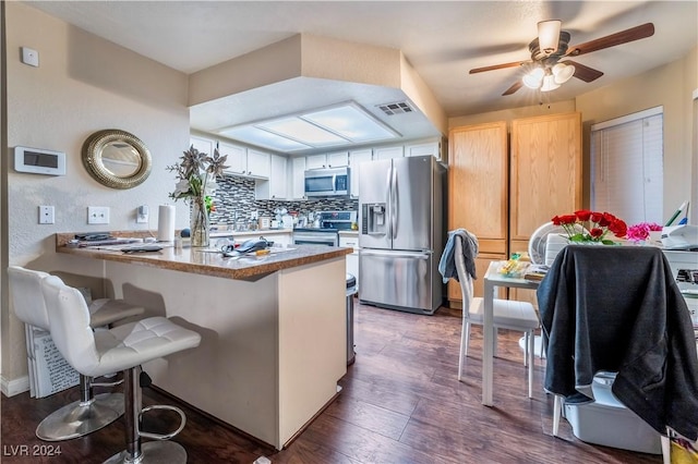 kitchen with dark wood-type flooring, white cabinets, a breakfast bar area, kitchen peninsula, and stainless steel appliances