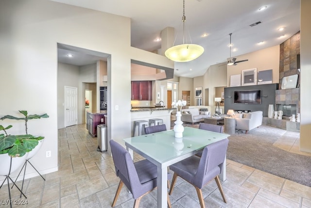 dining space with ceiling fan, high vaulted ceiling, and a tile fireplace