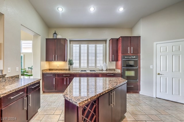 kitchen with multiple ovens, a center island, gas stovetop, light stone countertops, and a healthy amount of sunlight