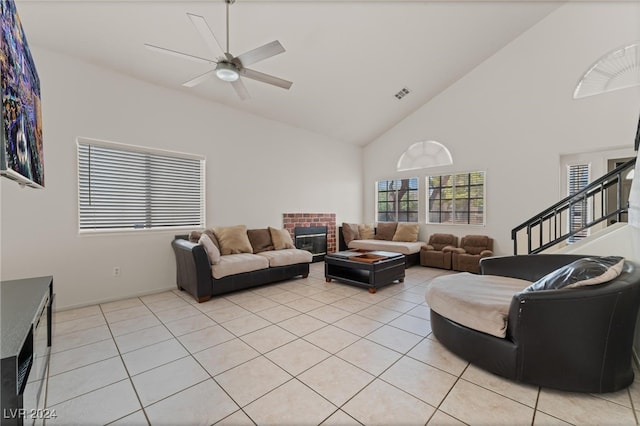 living room featuring light tile patterned floors, high vaulted ceiling, ceiling fan, and a brick fireplace