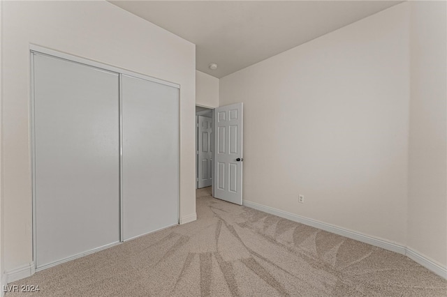 unfurnished bedroom with light colored carpet and a closet