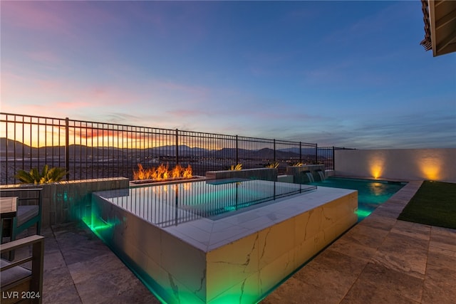 pool at dusk featuring pool water feature and a hot tub