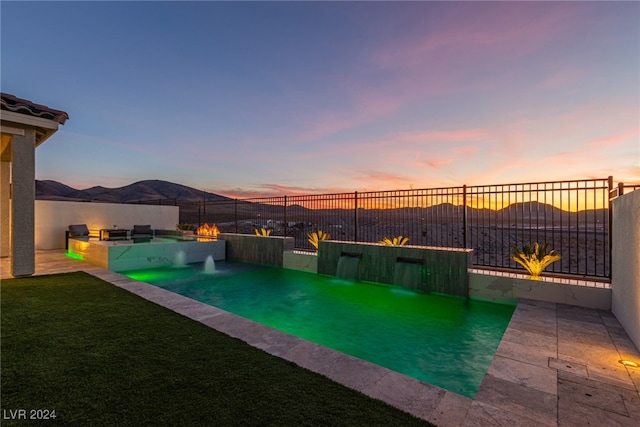 pool at dusk featuring a mountain view and an outdoor kitchen