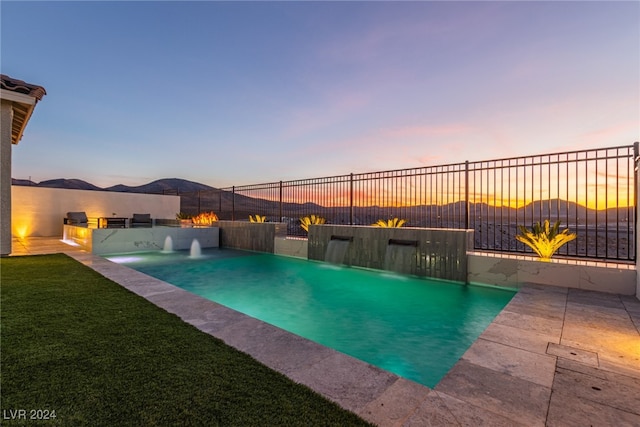 pool at dusk featuring pool water feature, an outdoor kitchen, a patio area, and a mountain view