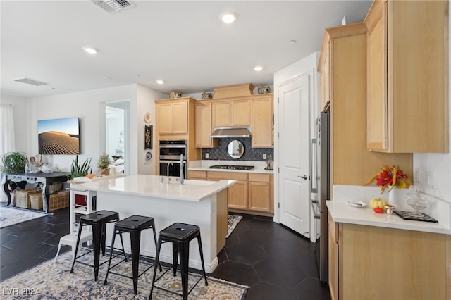 kitchen featuring gas cooktop, a breakfast bar, stainless steel double oven, a kitchen island with sink, and light brown cabinets