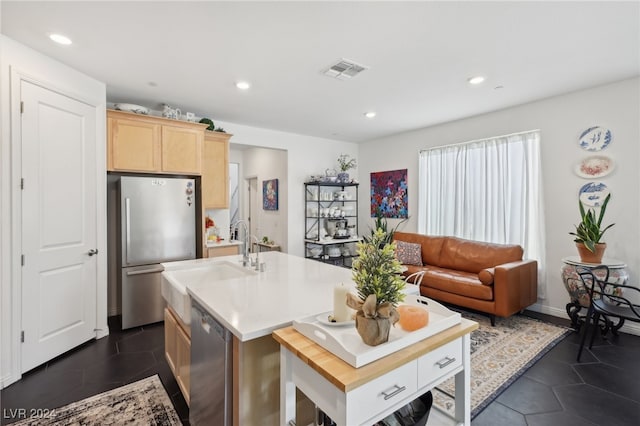 kitchen with sink, dark tile patterned floors, a kitchen island with sink, light brown cabinetry, and appliances with stainless steel finishes