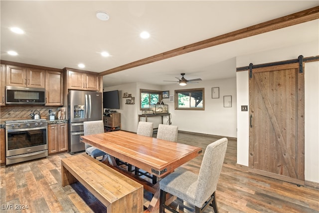 dining room with a ceiling fan, a barn door, light wood-style flooring, and recessed lighting