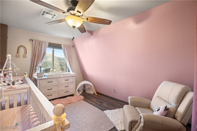 bedroom featuring visible vents, a crib, a ceiling fan, and dark wood-style flooring