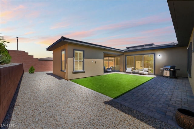 back house at dusk featuring outdoor lounge area, a patio, and a lawn