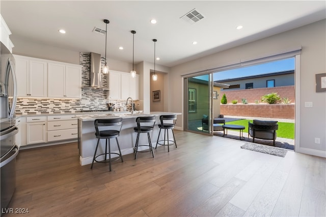 kitchen with an island with sink, white cabinetry, hardwood / wood-style flooring, and wall chimney range hood