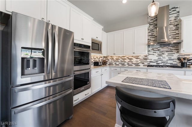 kitchen featuring light stone counters, white cabinets, wall chimney range hood, and appliances with stainless steel finishes