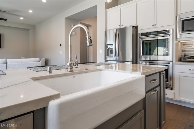 kitchen featuring light stone countertops, appliances with stainless steel finishes, dark hardwood / wood-style flooring, sink, and white cabinetry