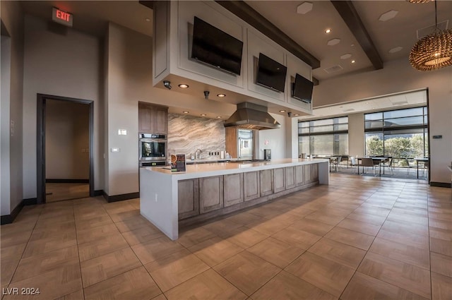 kitchen with tasteful backsplash, ventilation hood, sink, pendant lighting, and a large island