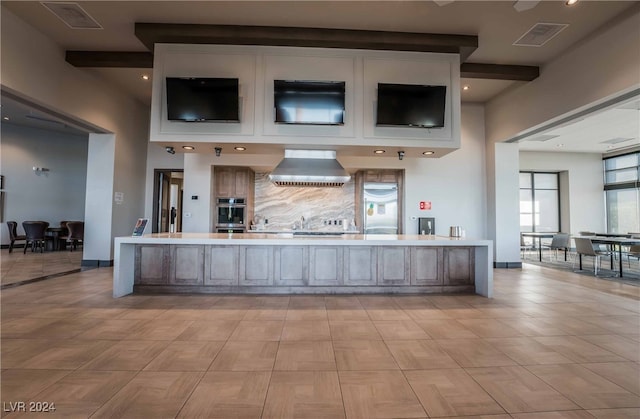 kitchen with double oven, a center island, wall chimney exhaust hood, and beam ceiling