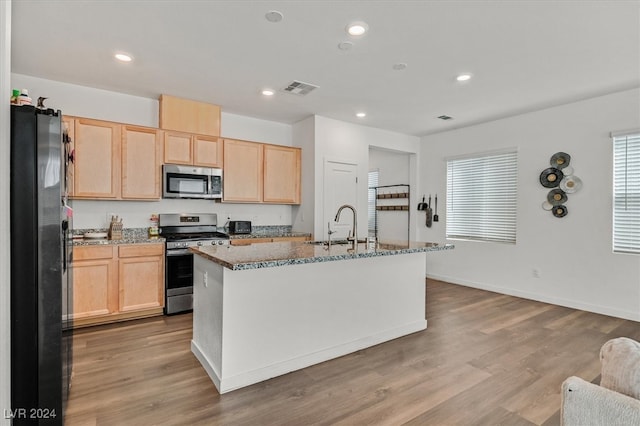 kitchen with light stone counters, an island with sink, stainless steel appliances, and light wood-type flooring