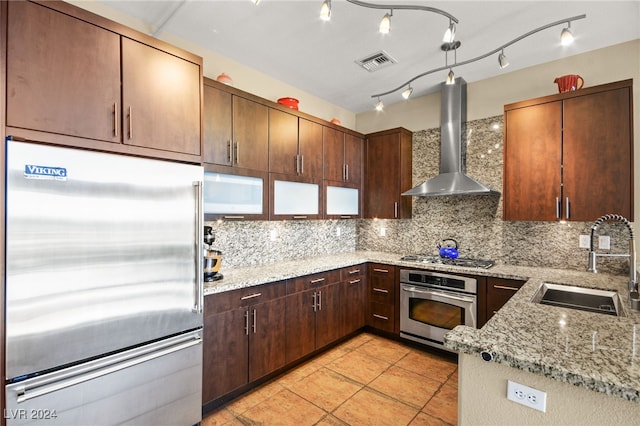 kitchen with tasteful backsplash, light stone counters, wall chimney exhaust hood, stainless steel appliances, and sink