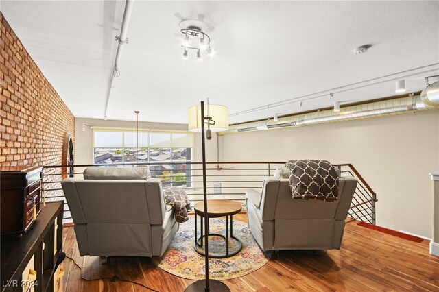 living room with hardwood / wood-style floors, rail lighting, and brick wall