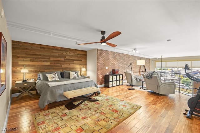 bedroom with brick wall, light hardwood / wood-style flooring, ceiling fan, and wood walls