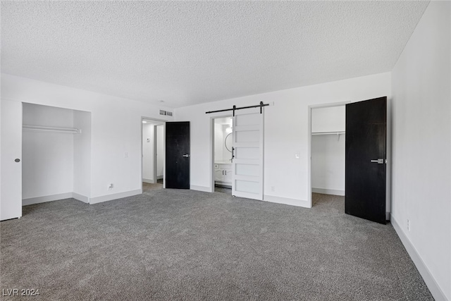 unfurnished bedroom featuring a barn door, carpet, and a textured ceiling