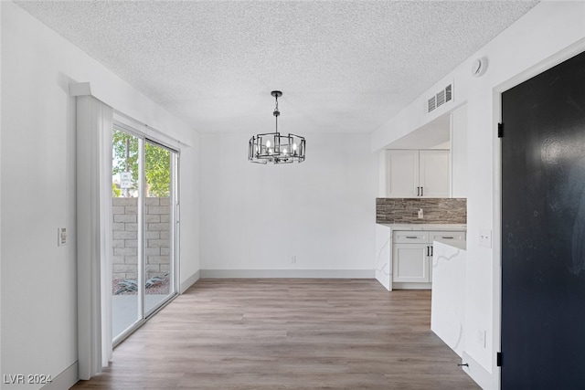 unfurnished dining area with a chandelier, a textured ceiling, and light hardwood / wood-style flooring