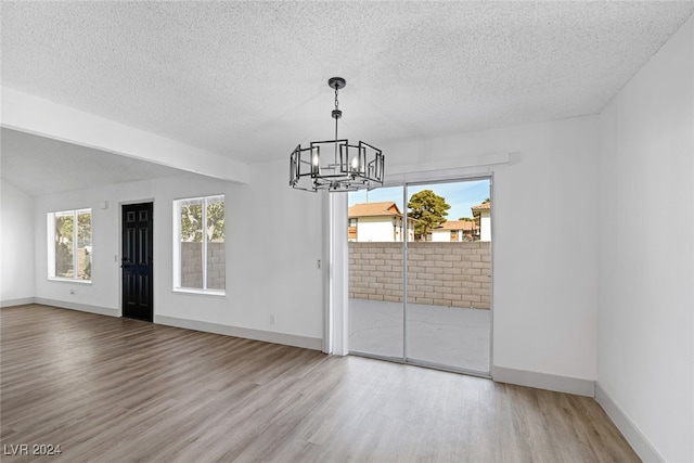 unfurnished dining area featuring a textured ceiling, hardwood / wood-style flooring, and an inviting chandelier