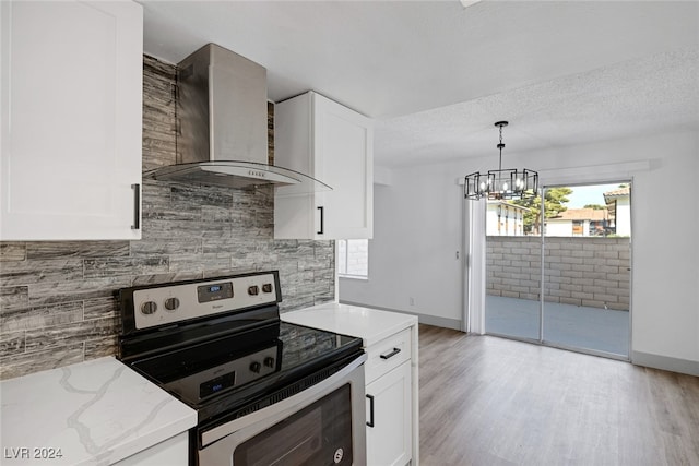 kitchen with white cabinetry, wall chimney exhaust hood, light stone counters, light hardwood / wood-style floors, and electric stove