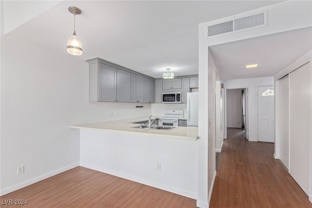 kitchen with kitchen peninsula, white appliances, sink, pendant lighting, and hardwood / wood-style floors