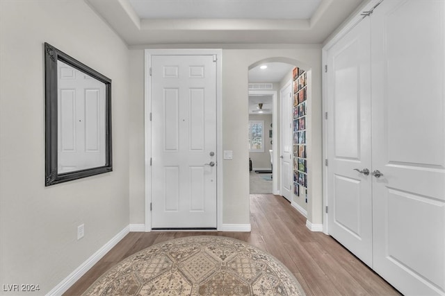 entryway featuring light wood-type flooring, ceiling fan, and a tray ceiling