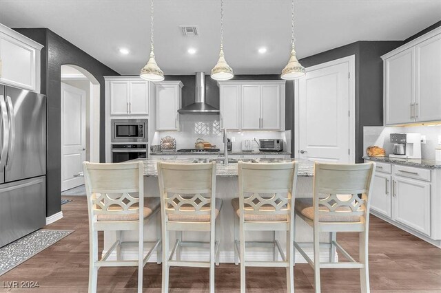 kitchen featuring wall chimney exhaust hood, light stone counters, hanging light fixtures, and stainless steel appliances