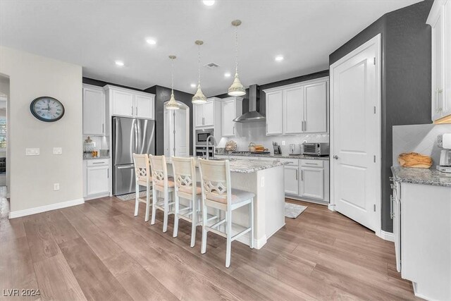 kitchen featuring pendant lighting, appliances with stainless steel finishes, wall chimney exhaust hood, white cabinetry, and decorative backsplash