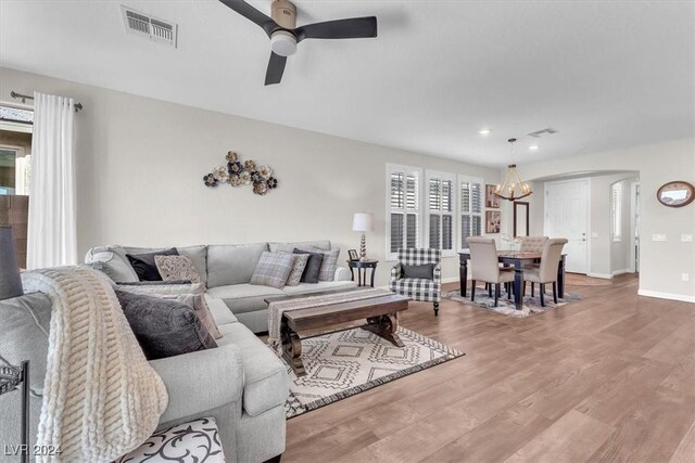 living room with light wood-type flooring and ceiling fan with notable chandelier