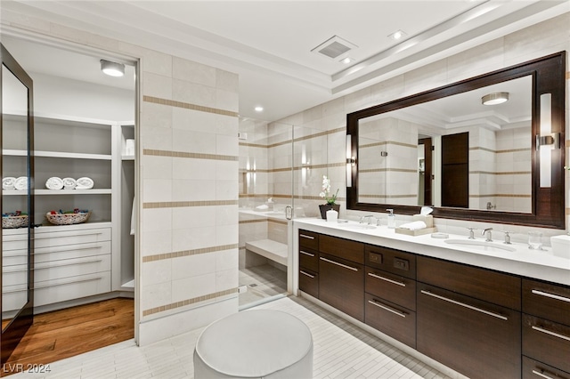 bathroom with wood-type flooring, vanity, a shower with shower door, tile walls, and ornamental molding