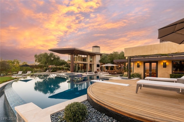 pool at dusk with an in ground hot tub, french doors, and a patio