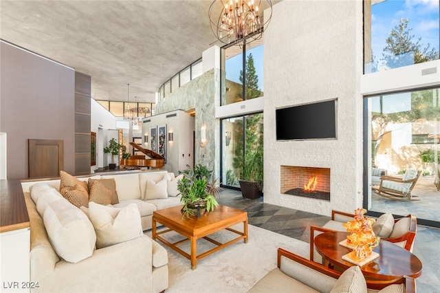 living room featuring a stone fireplace, a high ceiling, and a notable chandelier