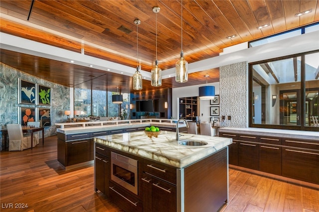 kitchen featuring stainless steel microwave, sink, a center island with sink, hardwood / wood-style flooring, and hanging light fixtures