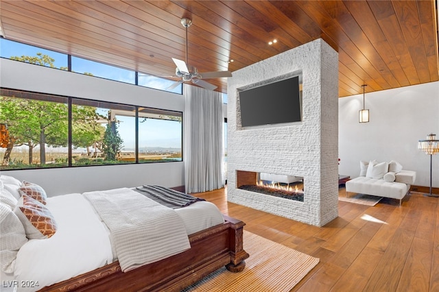 bedroom with vaulted ceiling, ceiling fan, a fireplace, wood-type flooring, and wood ceiling