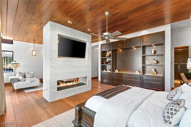 bedroom with a stone fireplace, ceiling fan, wood ceiling, and wood-type flooring