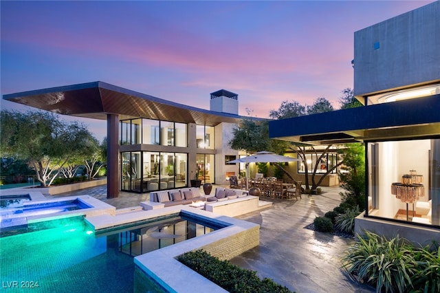 back house at dusk featuring a swimming pool with hot tub, a patio area, and an outdoor hangout area