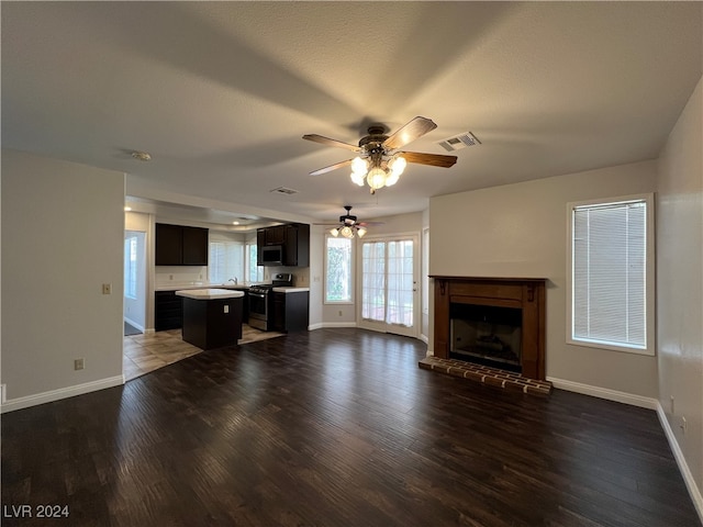 unfurnished living room with a textured ceiling, ceiling fan, dark hardwood / wood-style floors, and a brick fireplace