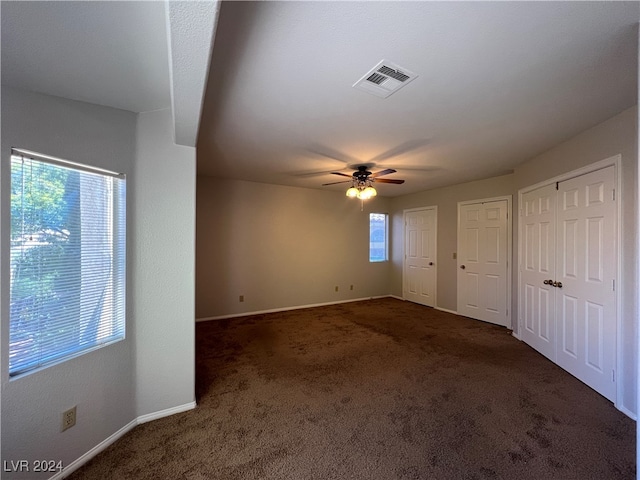 unfurnished bedroom with dark carpet, multiple closets, and multiple windows