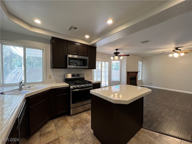 kitchen with tile countertops, ceiling fan, sink, and appliances with stainless steel finishes