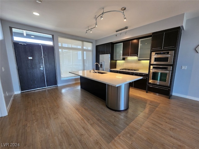 kitchen with sink, backsplash, a center island with sink, appliances with stainless steel finishes, and hardwood / wood-style flooring