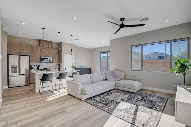 living room featuring light wood-type flooring, ceiling fan, and sink