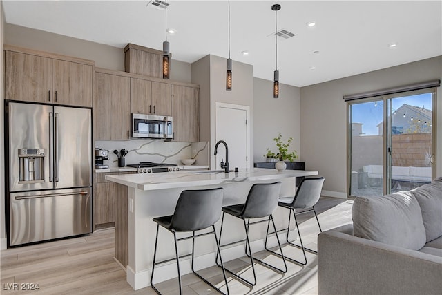 kitchen featuring sink, pendant lighting, a kitchen island with sink, appliances with stainless steel finishes, and light wood-type flooring